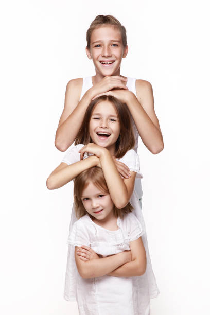 Three children in the studio on a white background, a brother and two sisters laugh, put their hands on each other 's head, stand the tower, indulge. Happy, healthy childhood.