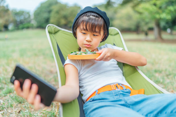 small girl eating vegan food outdoors and using smart phone - salad japanese culture japan asian culture imagens e fotografias de stock