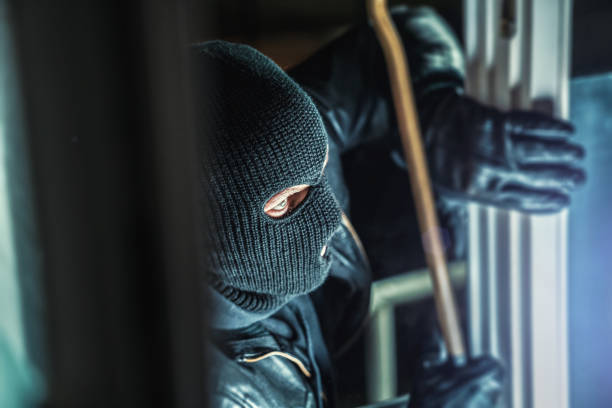 Masked burglar with torch and crowbar breaking and entering into a house - shot with dramatic motion