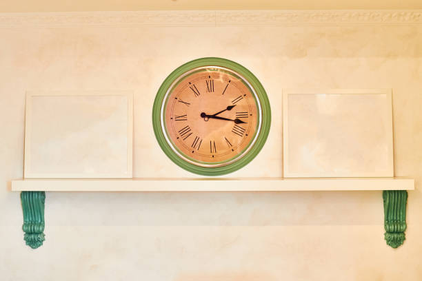 istock Wall clock on beige background. Shelf with frames from patterns and copy space. Green and brown color of the clock with Roman dial. 1178787932