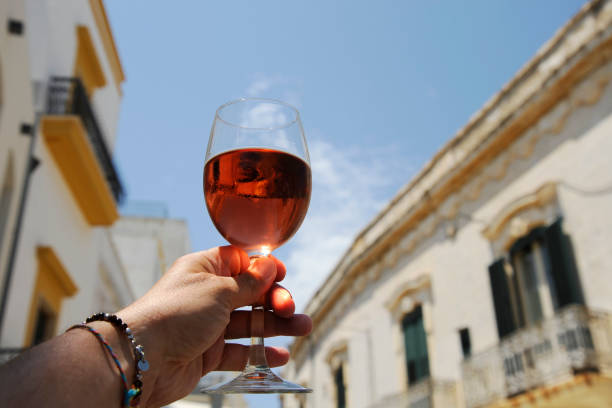 Glass of rose wine in man's hand against a blue sky background. Close-up. Relaxed mood concept in the historical italian city. Glass of rose wine in man's hand against a blue sky background. Close-up. Relaxed mood concept in the historical italian city. salento puglia stock pictures, royalty-free photos & images