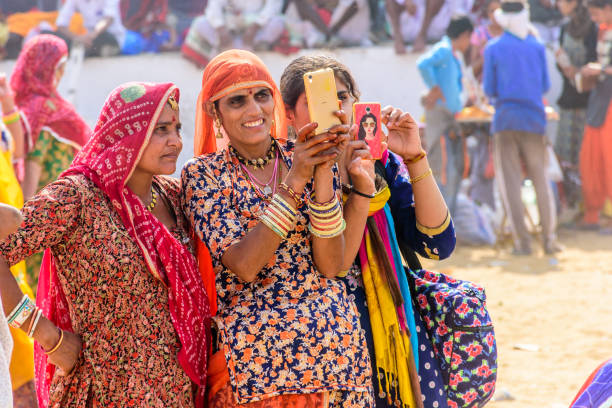 donne locali non identificate che indossano panni tradizionali si fanno selfie durante la fiera pushkar camel vicino alla città santa pushkar, rajasthan, india. - india travel journey camel foto e immagini stock