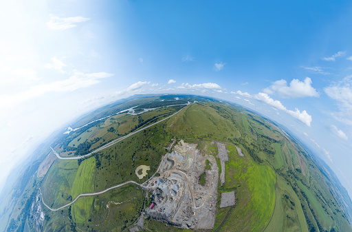 Aerial view 360 panoramic of opencast mining quarry minerals with many machinery tractors and trucks surrounded by green fields.