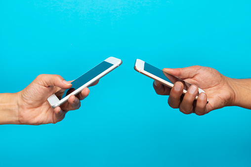 Man and woman holding smart phones on blue background.