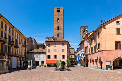 Cobblestone town square surrounded by typical colorful houses and medieval towers in Alba, Piedmont, Northern Italy.