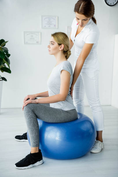 attractive patient sitting on blue exercise ball and chiropractor touching her back