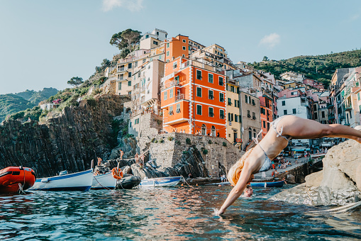 Woman in bikini dipping in water against buildings on cliff, Cinque Terre, Italy