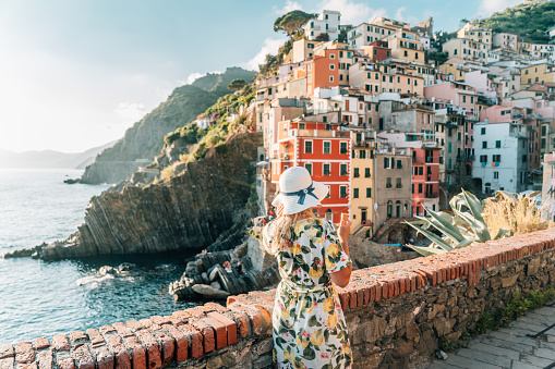 Rear view of woman in dress and hat standing against coastline, Cinque Terre, Italy