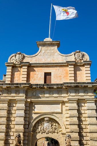 The Mdina flag flying above the main gate to the historic city of Mdina in Malta.  Mdina served as the capital of Malta from antiquity to the medieval period.