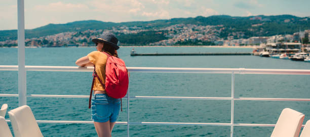 Girl leaning on metal fence at ferry looking at the sea Girl wearing sun hat and red backpack leaning on metal fence at ferry and looking at the sea ferry deck girls stock pictures, royalty-free photos & images
