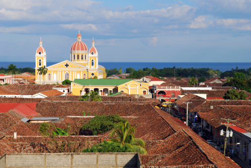 The skyline of Granada, Nicaragua, with its yellow cathedral, rooftops in Spanish colonial style architecture and Lake Nicaragua in the background.