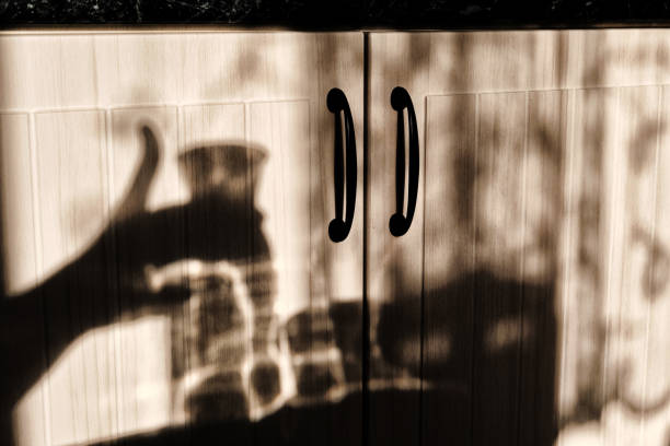 istock Shadows against the kitchen cabinet. Shadow hand on background kitchen. Cup and a decanter of water in the sun. 1178806110