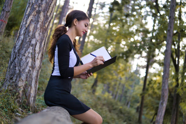 istock Side view of brunette woman sitting on large fallen tree and reading book. 1178806126