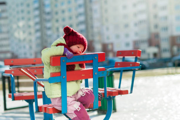 2-летняя девочка катается на карусели на свежем воздухе, в зимний холодный солнечный день. - playground snow winter little girls стоковые фото и изображения
