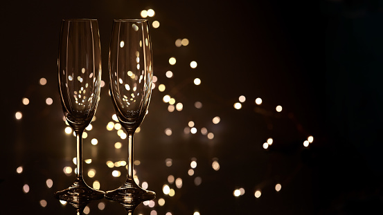 Two empty glasses for champagne on a dark background with LED lights garland. Copy space for text.