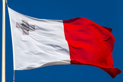 Maltese flag waving in the wind on the street with Aubrage de castille in the background in Malta.