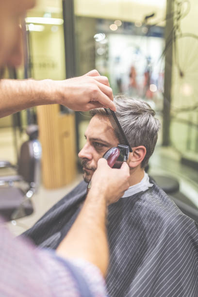 istock Professional barber styling hair of his client by using comb and clipper. 1178821869