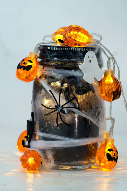 istock Jar filled with orange string lights in spooky room full in a black jar with a web and a spider on a light background 1178823684