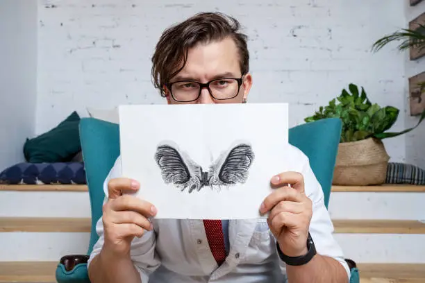 Photo of Serious professional  psychologist showing paper with Rorschach inkblot