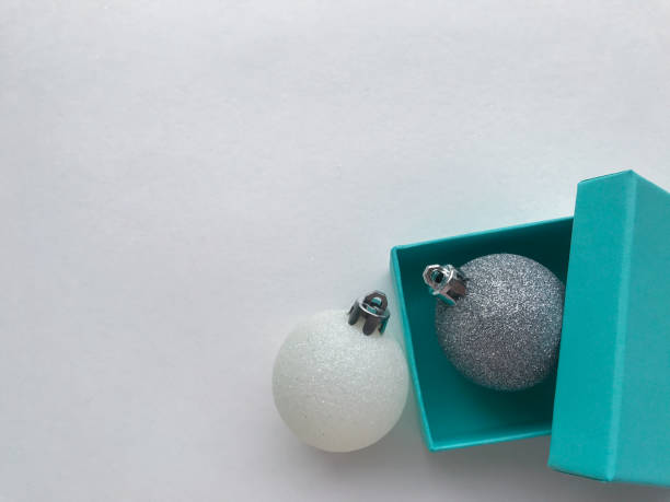 крупным планом бирюзовый (синий) подарочная коробка с блестящим рождественским шаром из серебра. рядом лежат бело-голубые. белый фон. дух пр - tiffany box стоковые фото и изображения