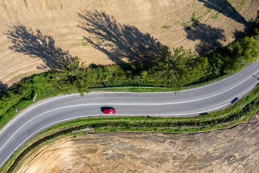 Red car driving down winding road, aerial view.