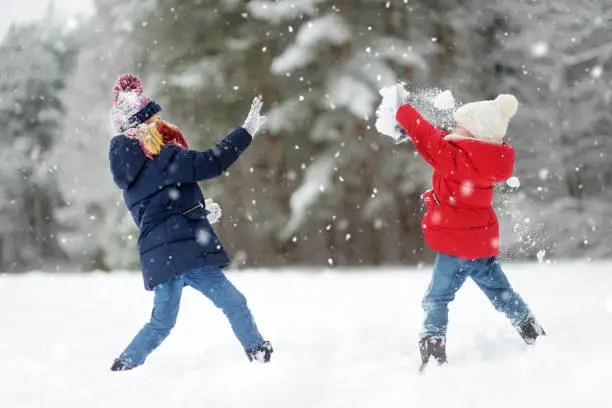 Photo of Two adorable little girls having fun together in beautiful winter park. Beautiful sisters playing in a snow.