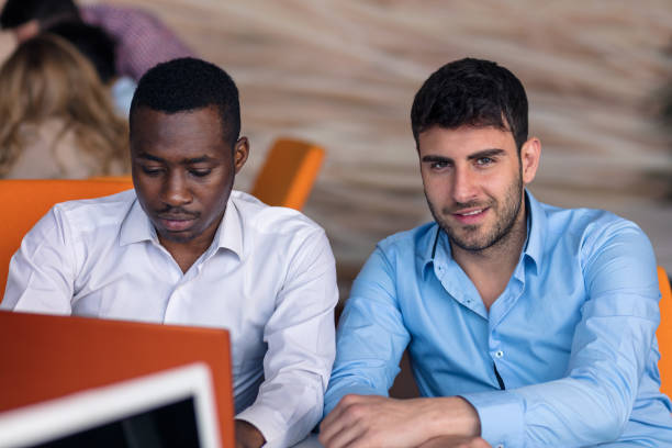 istock Two diverse work colleagues smiling while sitting together in an office discussing paperwork and working on a laptop 1178860086