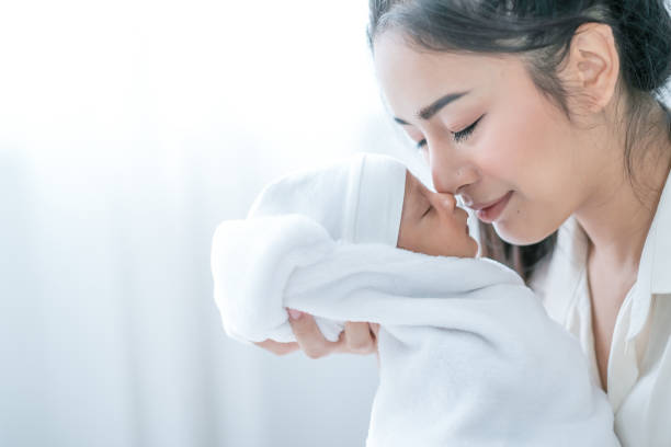 Close up shot of Asian mother kiss her newborn baby in front of white curtain in bedroom Close up shot of Asian mother kiss her newborn baby in front of white curtain in bedroom. forehead photos stock pictures, royalty-free photos & images