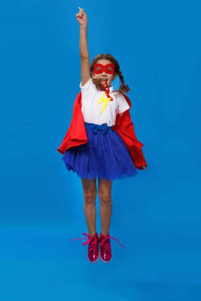 Little girl plays superhero jumping up. Kid on the background of bright blue wall. Girl power concept. stock photo