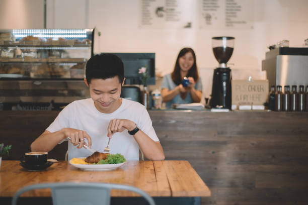 азиатский китайский мужчина клиент наслаждается своей едой в кафе с женщиной-владельцем позади на прилавке - smart casual occupation casual healthy eating стоковые фото и изображения
