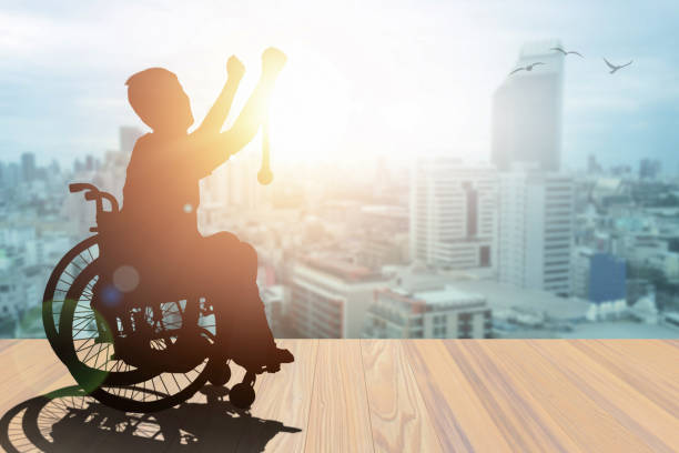 Disabled person silhouette winners hand holding gold medal top of wheelchair have sunset with city background. International Disability Day or Handicapped Paralympics. Challenge and Conquer concept.