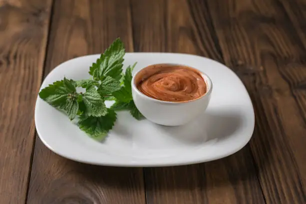 A sprig of fragrant grass and a red-and-white sauce on a wooden table. Vegetarian sauce. Sauce for meat and fish.