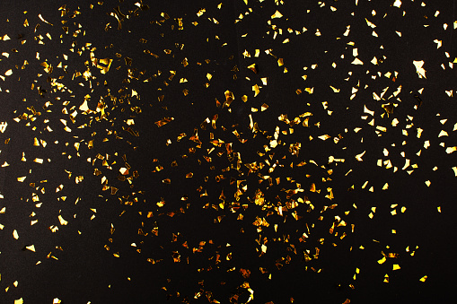 Falling gold foil confetti on black background. Celebration, New Year or Christmas concept.