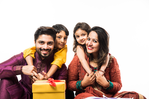Indian family celebrating Diwali / Deepavali in traditional wear while sitting isolated over white background with gift boxes and lamp in thali