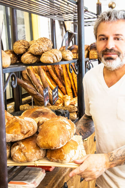 baker doing the restocking in his shop with a batch of cereal bread just coming out of the oven - adult variation boutique occupation imagens e fotografias de stock