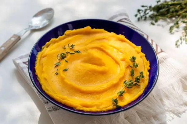 Autumn pumpkin puree in bowl. Autumnal pumpkin cream soup with thyme on white table. Autumn tasty vegetarian food. Top view