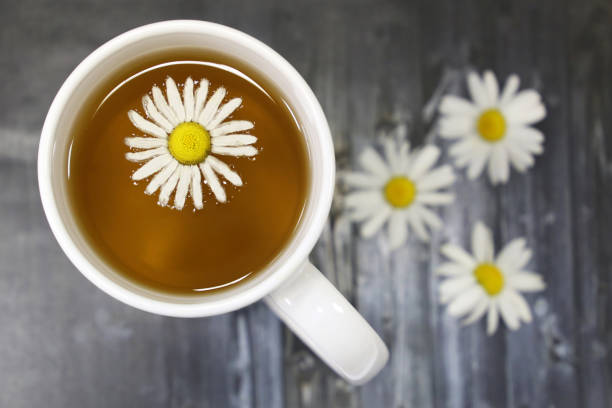 té de manzanilla en una taza blanca y flores margarita sin mesa oscura - manzanilla fotografías e imágenes de stock