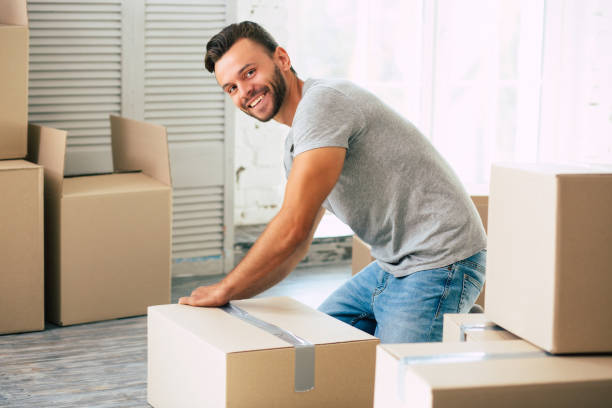 In the process of relocation. Happy bearded man is packing cardboard box in his new apartment. stock photo