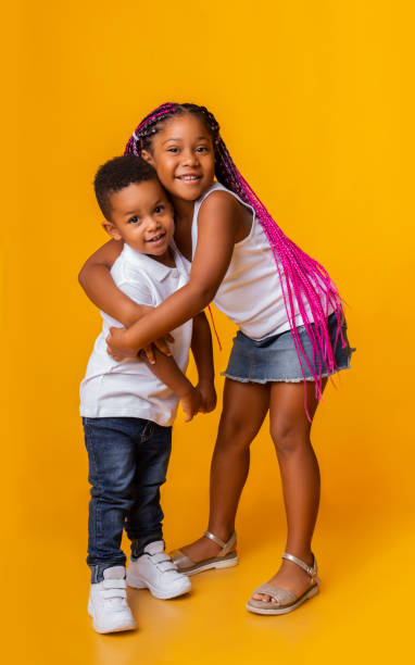 little brother and sister hugging and smiling on yellow background - african ethnicity brother ethnic little boys imagens e fotografias de stock