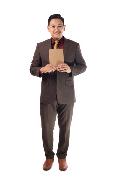 Full body portrait of a happy successful young Asian businessman smiling while holding a book, isolated on white