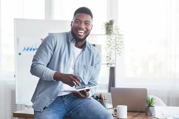 Photo of Cheerful black employee using digital tablet in office and laughing