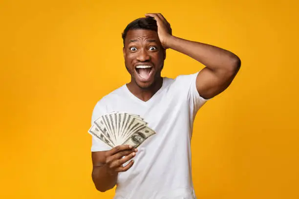 Photo of Excited Afro Guy Holding Money Shouting Touching Head, Yellow Background