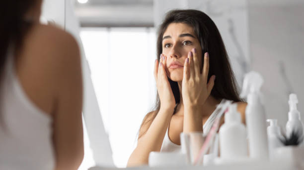 mujer tocando la cara mirando la piel en el espejo en el baño - wrinkle treatment fotografías e imágenes de stock