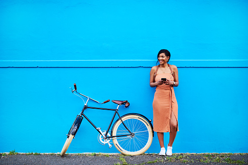 Full length shot of an attractive young woman using a cellphone while standing next to her bicycle outdoors