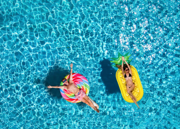 Couple on inflatable floats over blue pool water An attractive couple enjoys the hot summer day on colorful, inflatable floats over blue pool water inflatable photos stock pictures, royalty-free photos & images