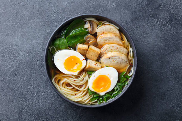 sopa de fideos asiáticos, ramen con pollo, tofu, verduras y huevo en tazón negro. vista superior. copiar espacio. fondo de pizarra. - soup chicken soup chicken noodle soup food fotografías e imágenes de stock