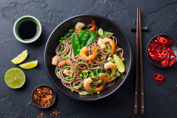 revuelva los fideos con verduras y camarones en un tazón negro. fondo de pizarra. vista superior. - wok fotografías e imágenes de stock