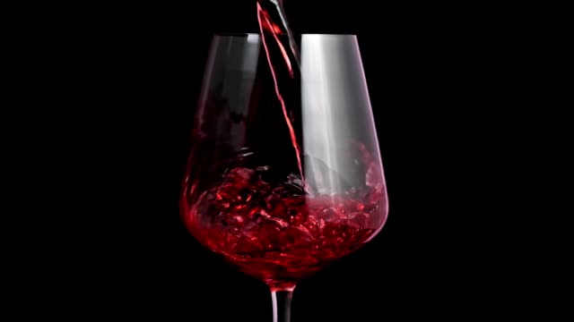 Pouring red wine into goblet. Close-up of red wine forms beautiful wave in glass