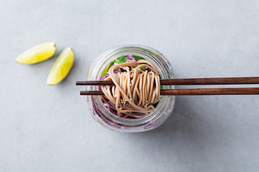 Noodles soba salad, soup with vegetables, tofu and chicken in jars. Grey background. Top view