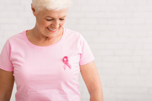 elderly woman looking at pink cancer ribbon on t-shirt, indoor - t shirt shirt pink blank imagens e fotografias de stock